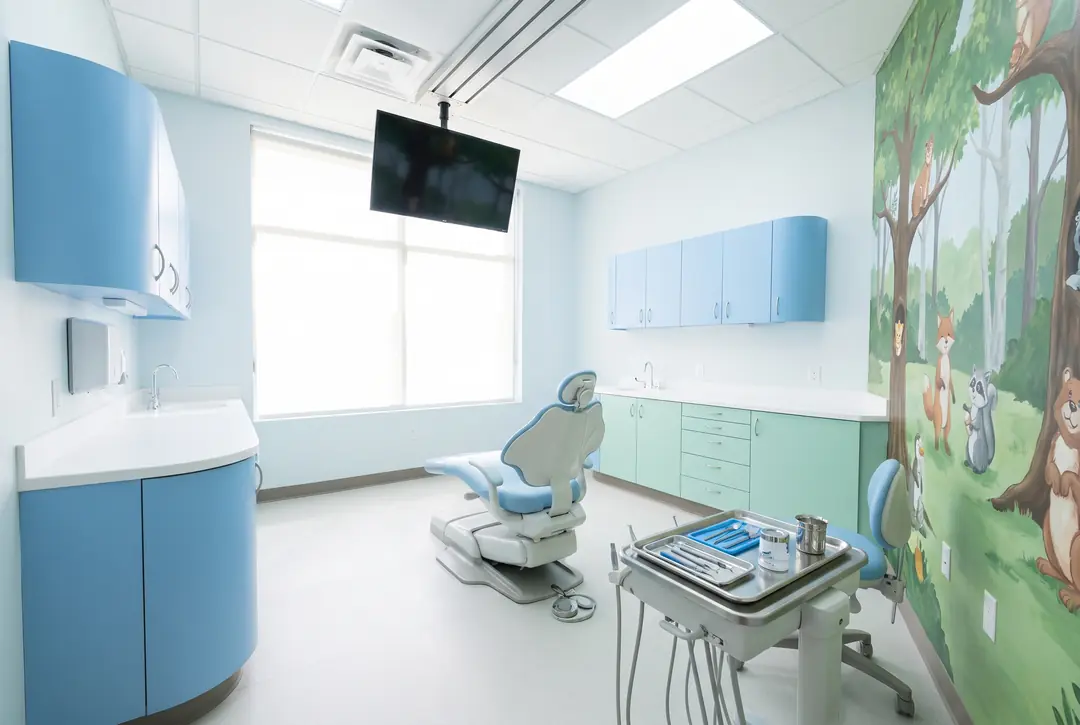 A children's dental treatment room with rounded sky-blue cabinetry, a ceiling-mounted screen above the chair and a painted forest mural